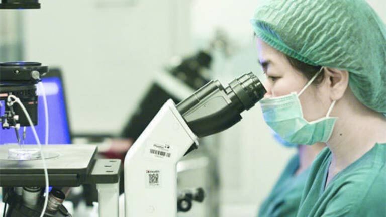 female Singaporean scientist looking at energy booster supplement through microscope